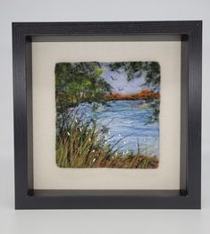 a painting with water and trees in the background, framed on white paper by a black frame