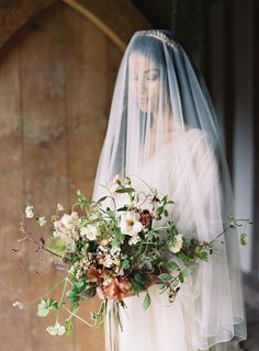 a bride holding a bouquet of flowers in front of her wedding dress with the veil pulled back