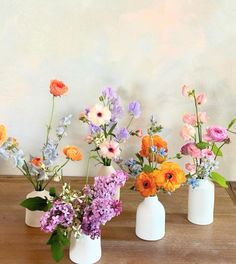 three white vases filled with different colored flowers