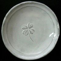 a white plate with a four - leaf clover design on the front and bottom, sitting on a black surface