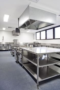 an empty commercial kitchen with stainless steel counters and appliances on the walls, along with blue carpeted flooring