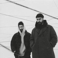 two men standing next to each other in front of power lines with one wearing a hoodie