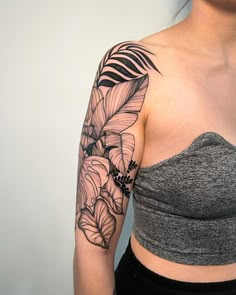 a woman's arm with flowers and leaves tattoo on her left shoulder, next to a white wall