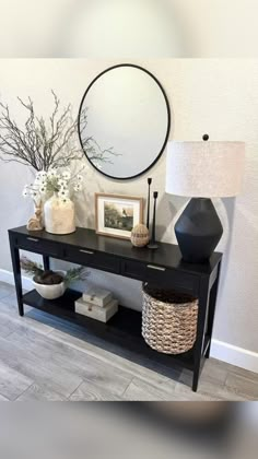 a black console table with two vases and a round mirror on the wall behind it