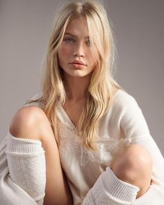 a woman with long blonde hair sitting on the ground wearing white sweaters and gloves