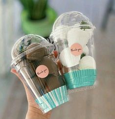 a person holding two plastic cups filled with chocolates and marshmallow cupcakes