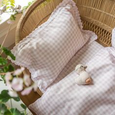 a wicker chair with two pillows and a stuffed animal on it next to some pink flowers