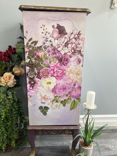 an easel with flowers painted on it next to a potted plant and candle