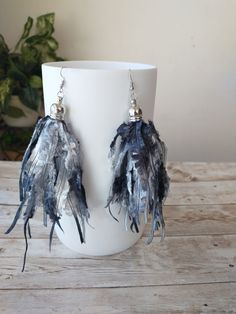 a pair of earrings with feathers hanging from them on a white cup sitting on a wooden table