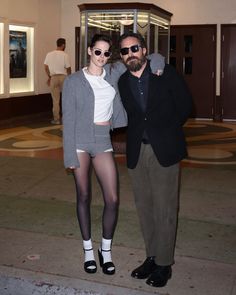 a man and woman standing next to each other in front of a building with doors