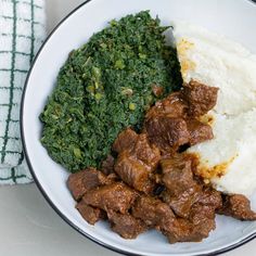 a white plate topped with meat and mashed potatoes next to spinach covered in gravy