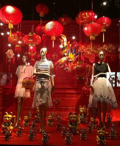 three mannequins dressed in dresses and headpieces with red lanterns hanging above them