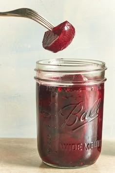 a spoon with some food in it next to a jar filled with red liquid and another jar full of jam