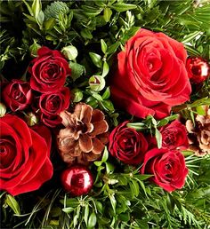 a bouquet of red roses with green leaves and berries on the bottom, surrounded by greenery