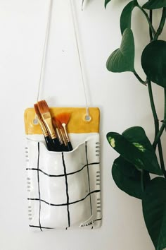 a white and yellow purse hanging on a wall next to a potted green plant