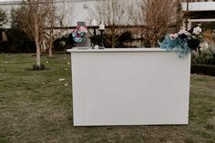 a white bar with flowers and candles on top in the grass next to some trees