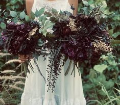 a woman in a white dress holding a bouquet of flowers and greenery with her hands