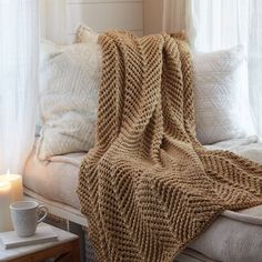 a knitted blanket sitting on top of a white couch next to pillows and windows