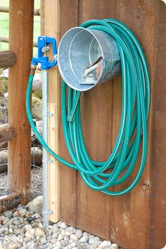 there is a bucket and hose attached to the side of a wooden structure with rocks around it