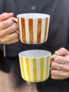 two people holding coffee mugs in their hands, one is yellow and the other is white