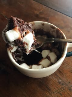 a spoon in a cup filled with chocolate and marshmallows on a wooden table