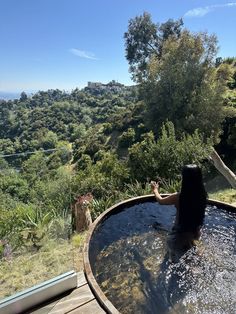 a woman sitting in an outdoor hot tub with trees and hills in the back ground