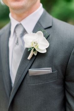 a man in a gray suit with a white flower on his lapel and tie