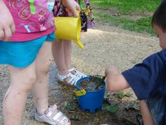 two children are playing with water in a blue bucket and another child is holding a yellow watering can