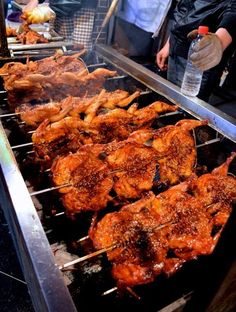 several skewers of food being cooked on a grill with people standing around them