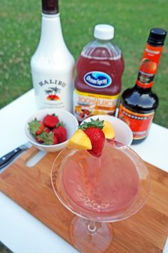 a drink in a glass with strawberries and lemon wedges next to it on a cutting board