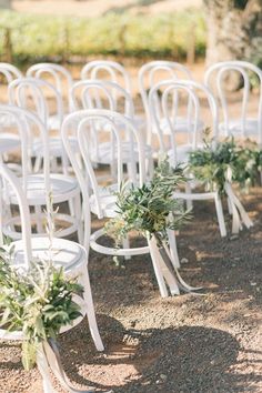 rows of white chairs with greenery tied to them