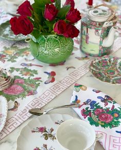 a table topped with plates and cups filled with red roses next to a green vase