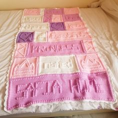 a pink and white crocheted blanket sitting on top of a bed