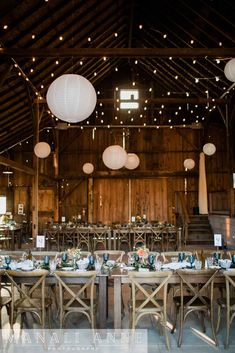 the tables are set up for an event with lanterns hanging from the ceiling and paper lanterns above them