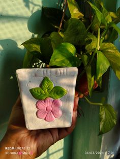 a hand holding a small ceramic planter with pink flowers on it's side