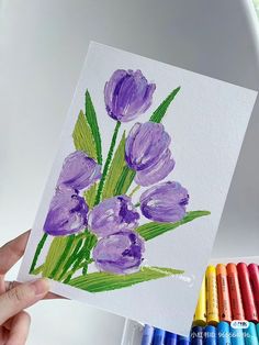 a person holding up a card with purple flowers on it and crayons next to it