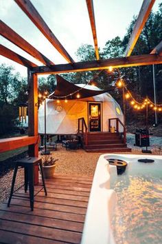 a hot tub sitting on top of a wooden deck next to a white tent covered in lights