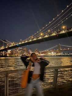 a man and woman standing next to each other near the water with a bridge in the background