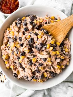 a white bowl filled with corn and black beans next to a wooden spoon on top of a table