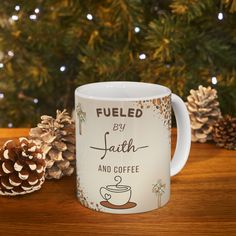 a white coffee mug sitting on top of a wooden table next to pine cones and christmas decorations