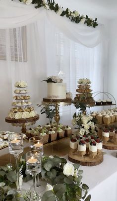 a table topped with cakes and cupcakes covered in frosting next to greenery