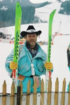 a man holding two skis standing next to a fence