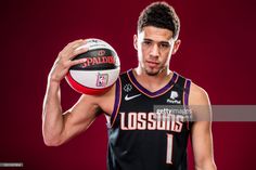 a basketball player holding a ball in his right hand and posing for a photo on a red