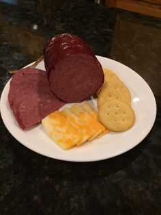 a white plate topped with meat, cheese and crackers on top of a table