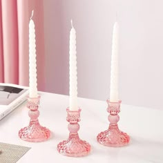 three pink candles sitting on top of a white table next to a book and phone