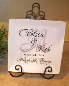 a white plate with a monogrammed wedding date on it sitting next to a pine tree