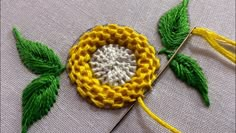 a crocheted flower with green leaves on it and yellow needles in the middle