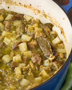 a blue pot filled with meat and potatoes on top of a stovetop next to green peppers