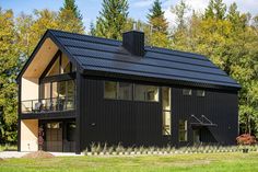 a black house in the middle of some trees and grass, with a balcony on top