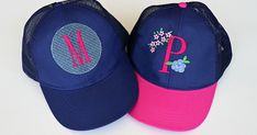 two blue and pink hats with flowers on the front, one has a monogrammed letter